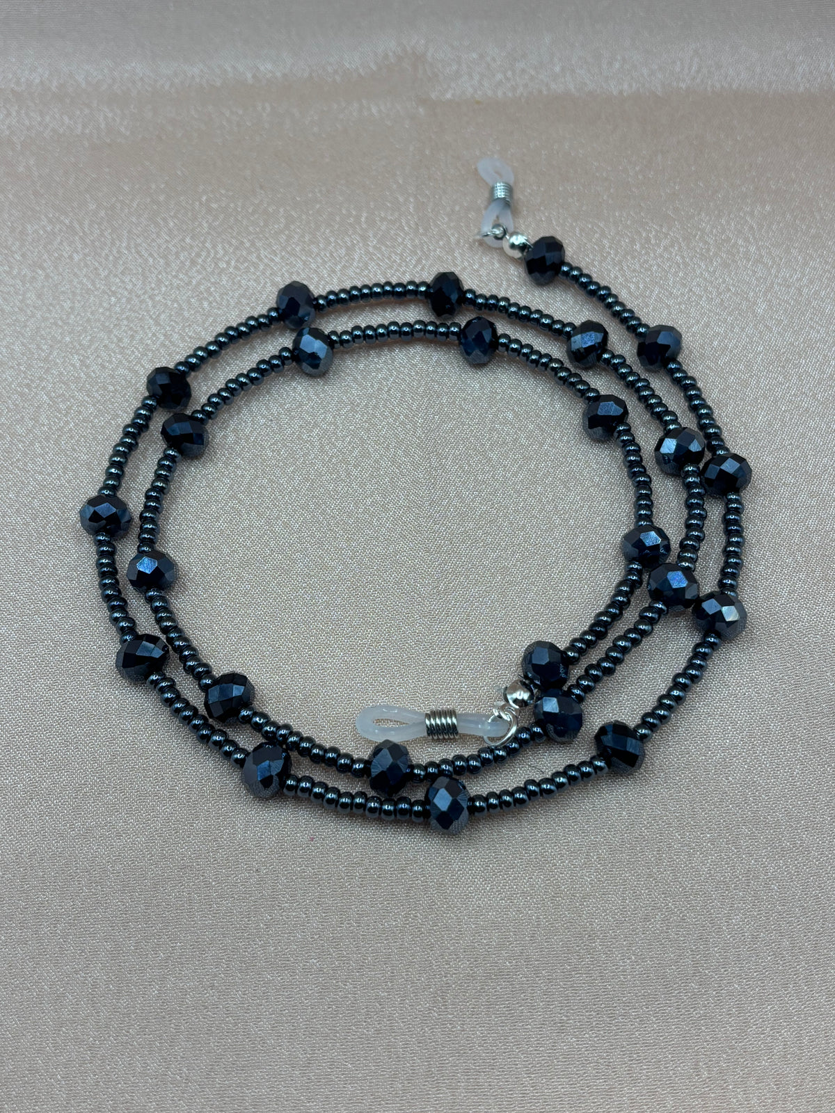 Black faceted crystal and metallic beaded eyeglass chain coiled on a pink background.