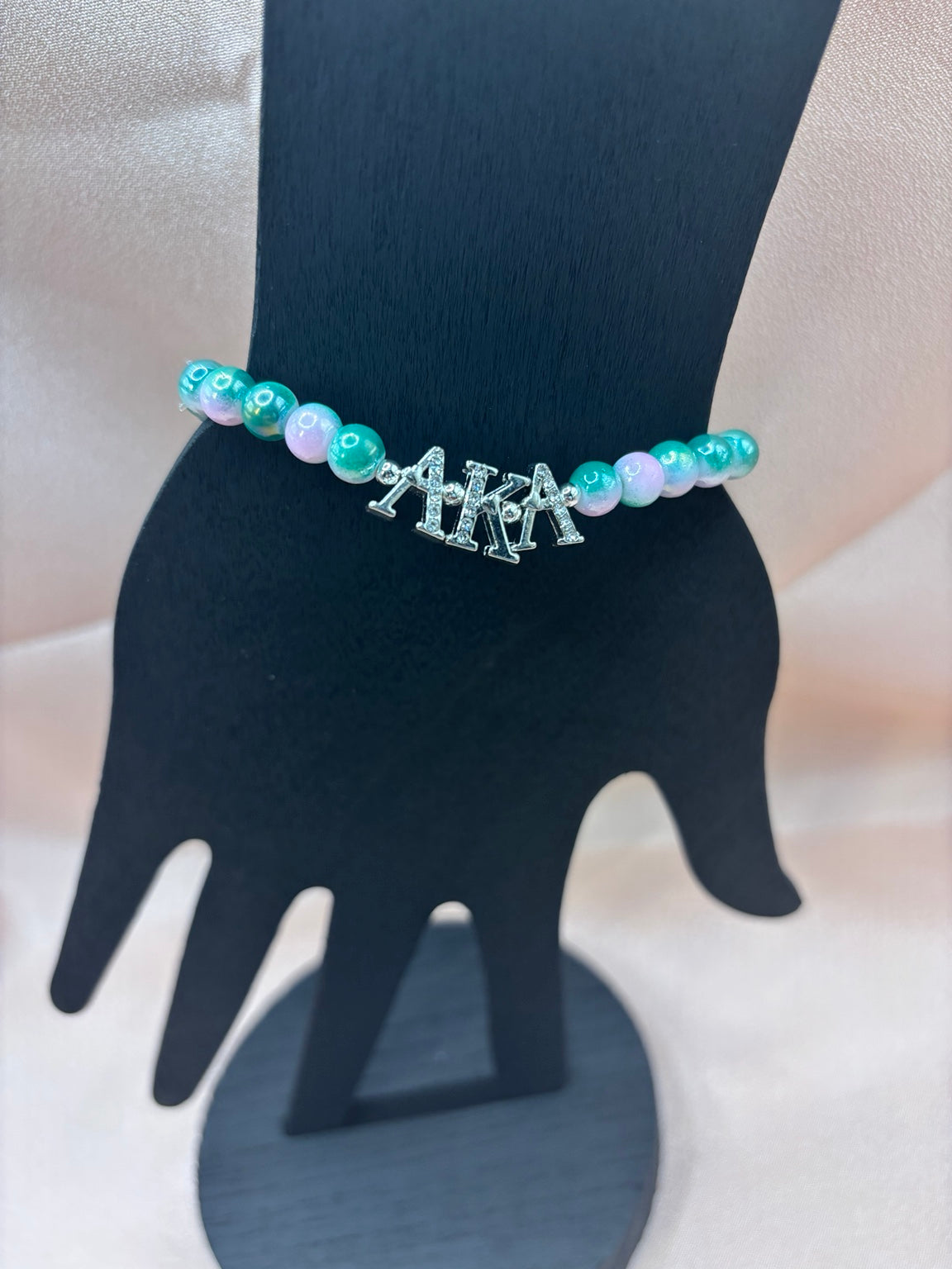 Alpha Kappa Alpha inspired sorority bracelet on a display hand featuring pink and green marbled beads with rhinestone-studded silver AKA Greek letter charms