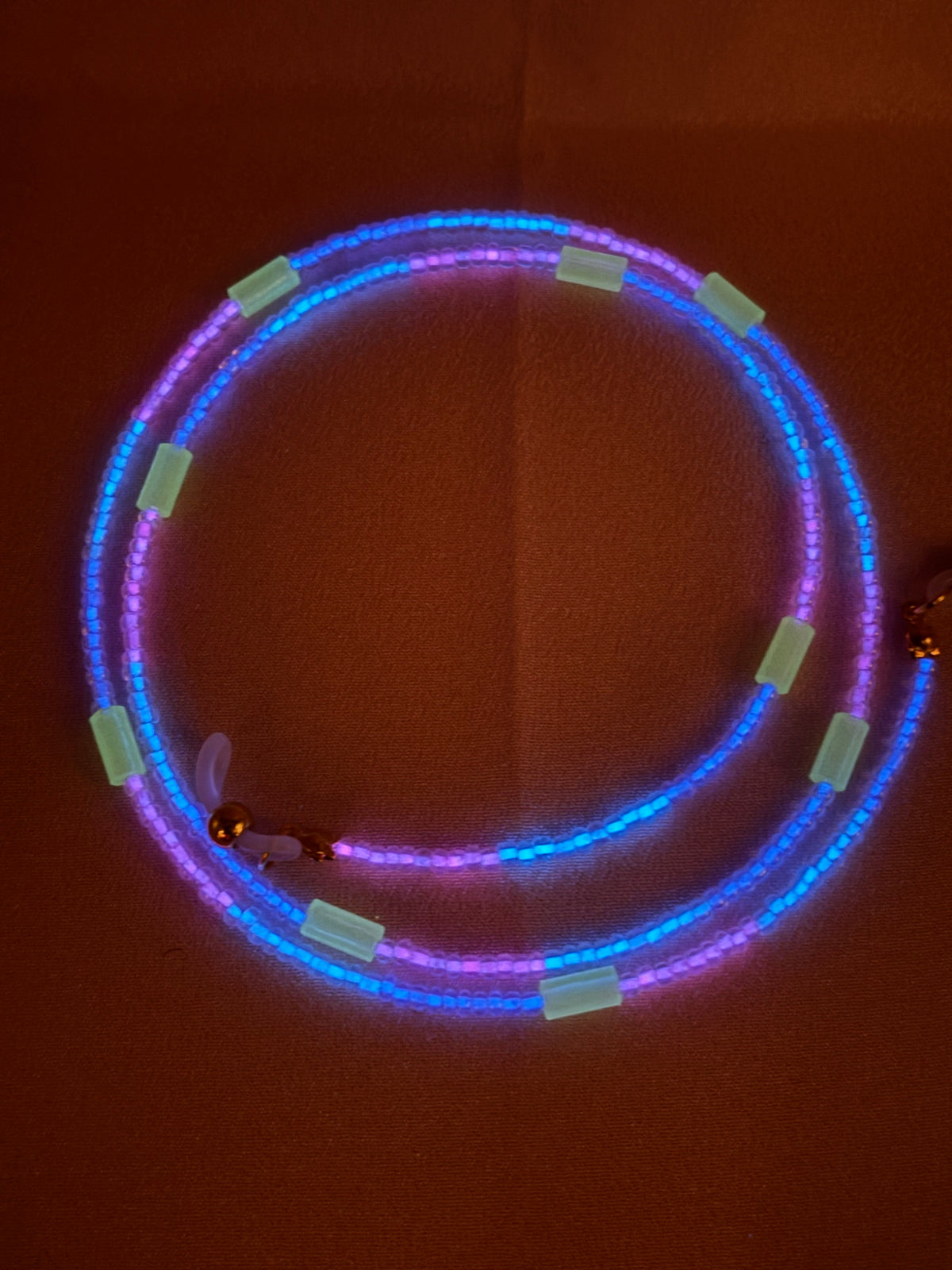 Vibrant blue and pink glow in the dark beaded necklace glowing in darkness.