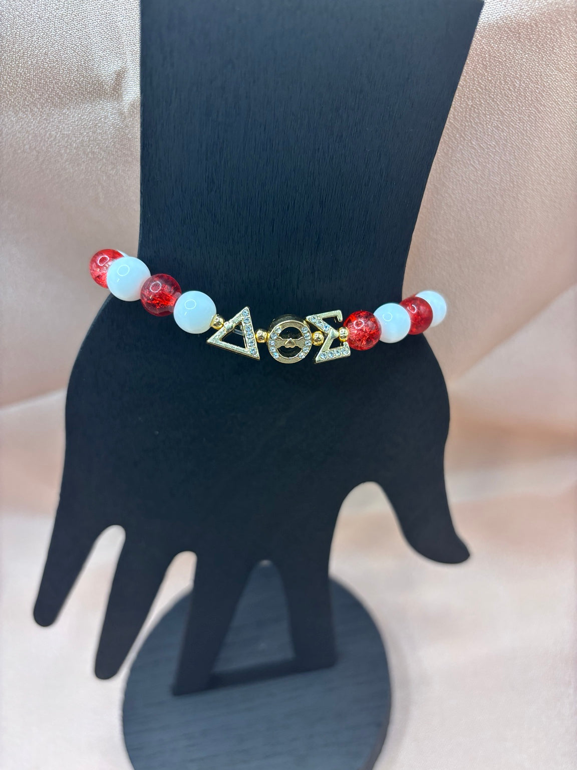 Delta Sigma Theta inspired sorority bracelet on a display hand featuring red crackle beads, solid white beads, and gold Greek letter charms