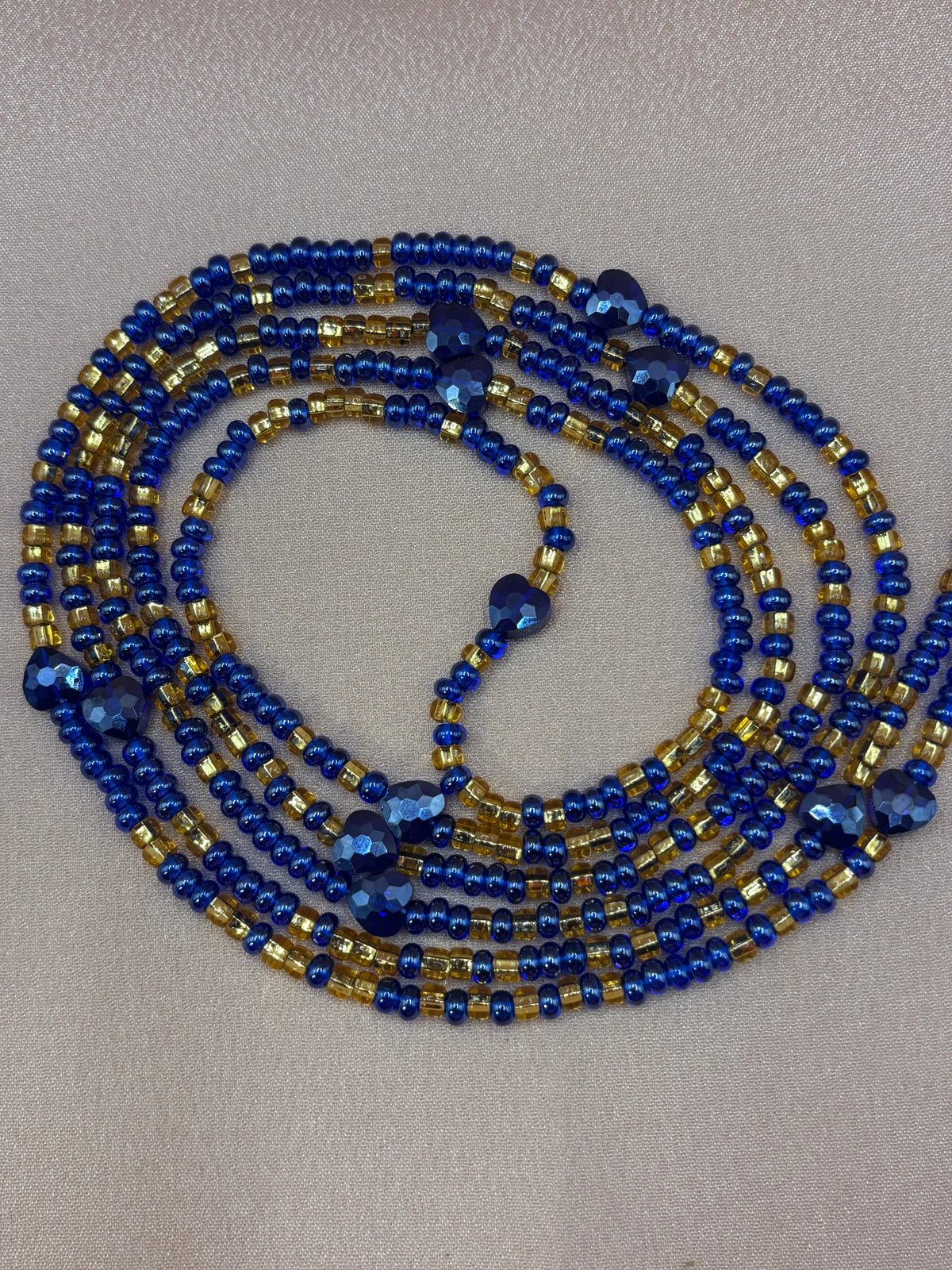 Her Majesty African waist beads featuring strands of deep royal blue and metallic gold seed beads with faceted dark blue heart-shaped accents.