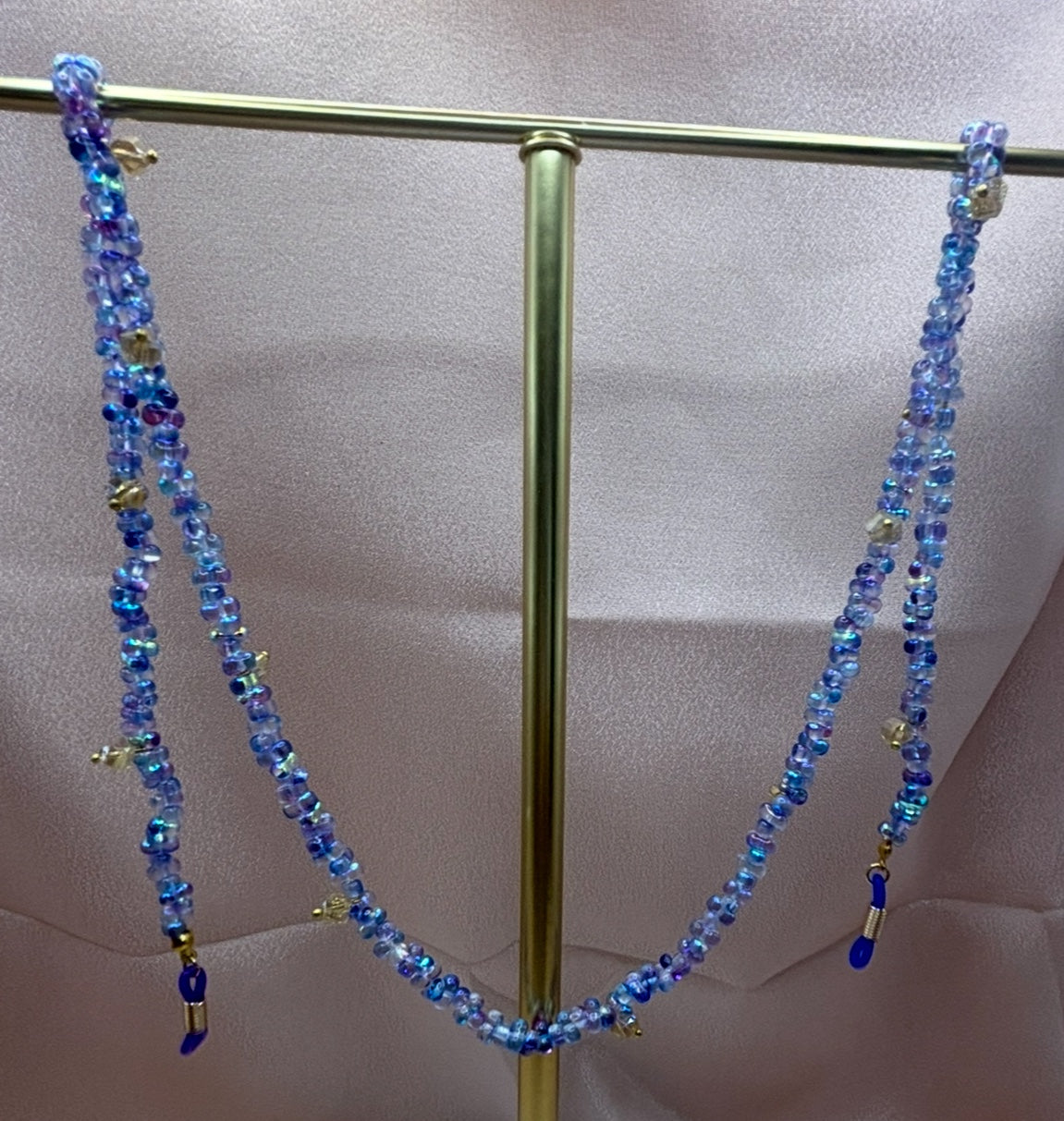 Beaded blue eyeglass chain with iridescent periwinkle and sea-blue  beads hanging on a gold display stand