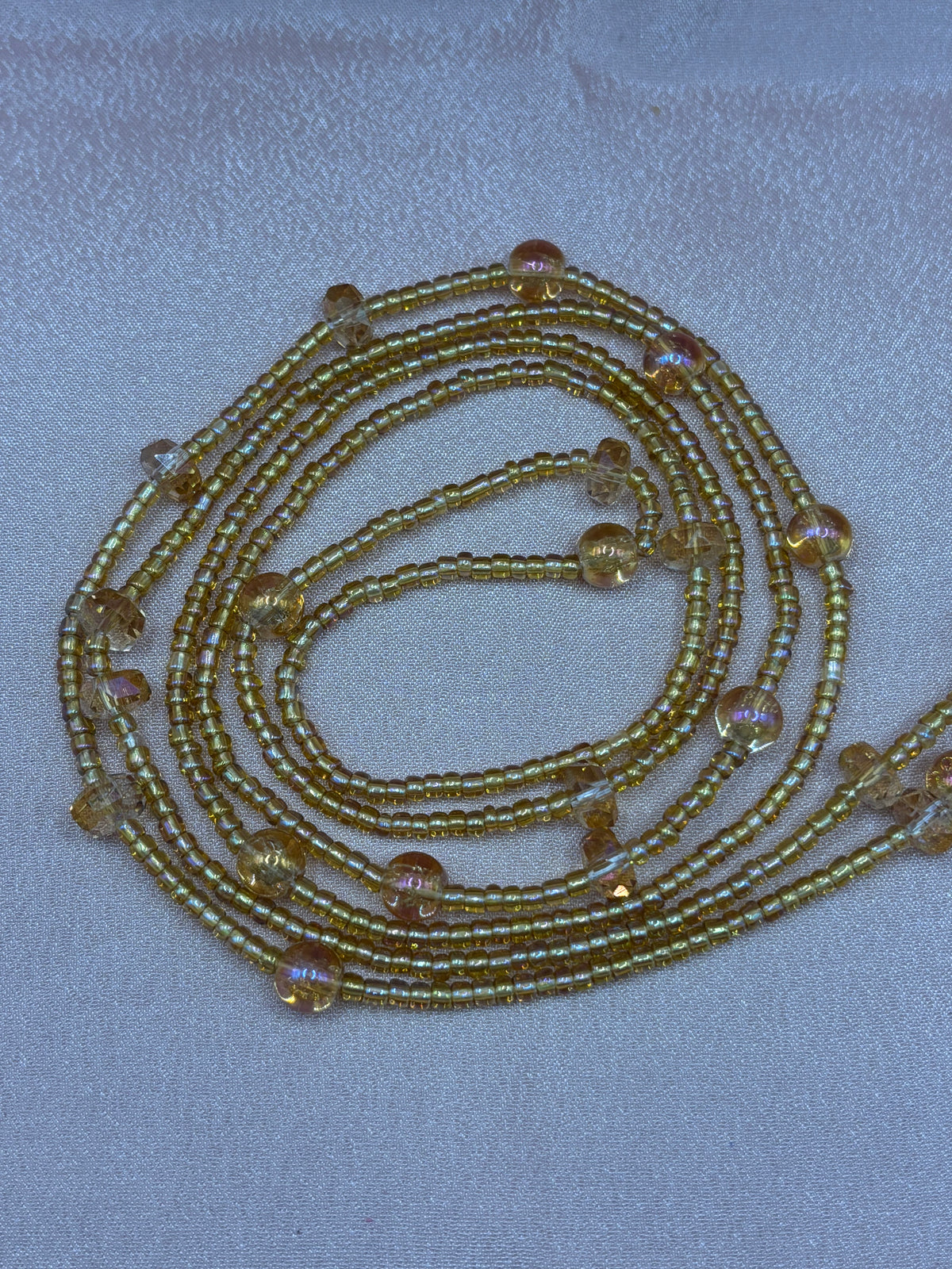 Goldilocks metallic gold beaded eyeglass chain with shimmering iridescent champagne accent beads coiled on a plain background.