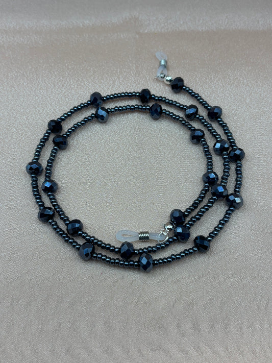 Black faceted crystal and metallic beaded eyeglass chain coiled on a pink background.