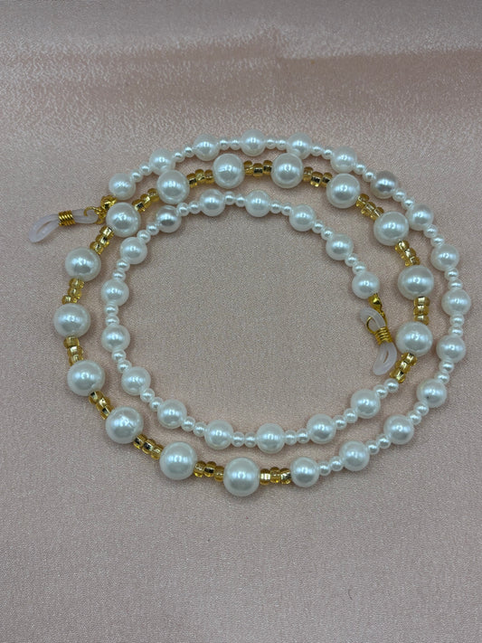 Elegant white pearl and gold beaded eyeglass chain coiled on a blush background.