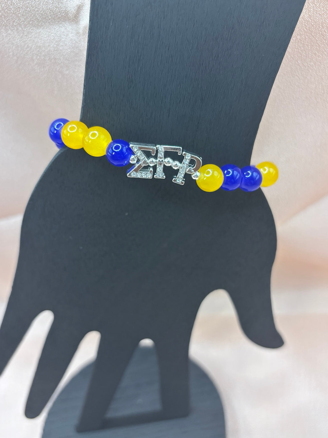 Sigma Gamma Rho inspired sorority bracelet on a display hand featuring royal blue and yellow beads with silver Greek letter charms