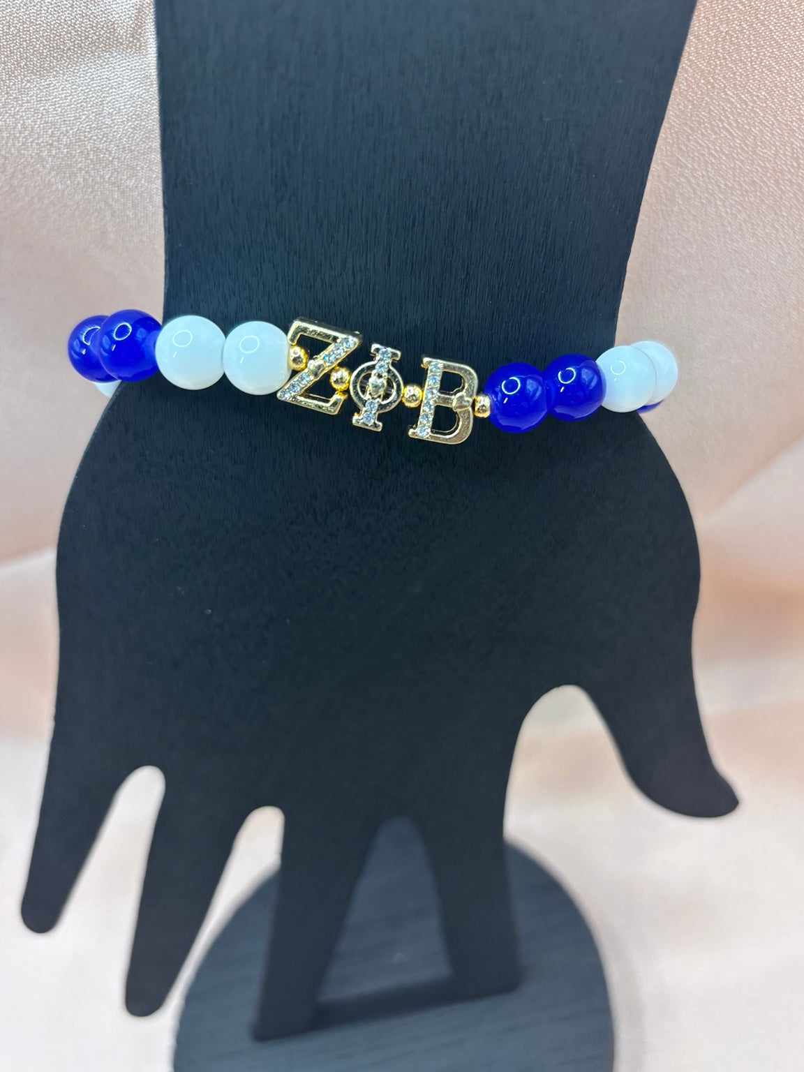 Zeta Phi Beta inspired sorority bracelet on a display hand featuring royal blue and solid white beads with rhinestone-studded gold ZPB Greek letter charms