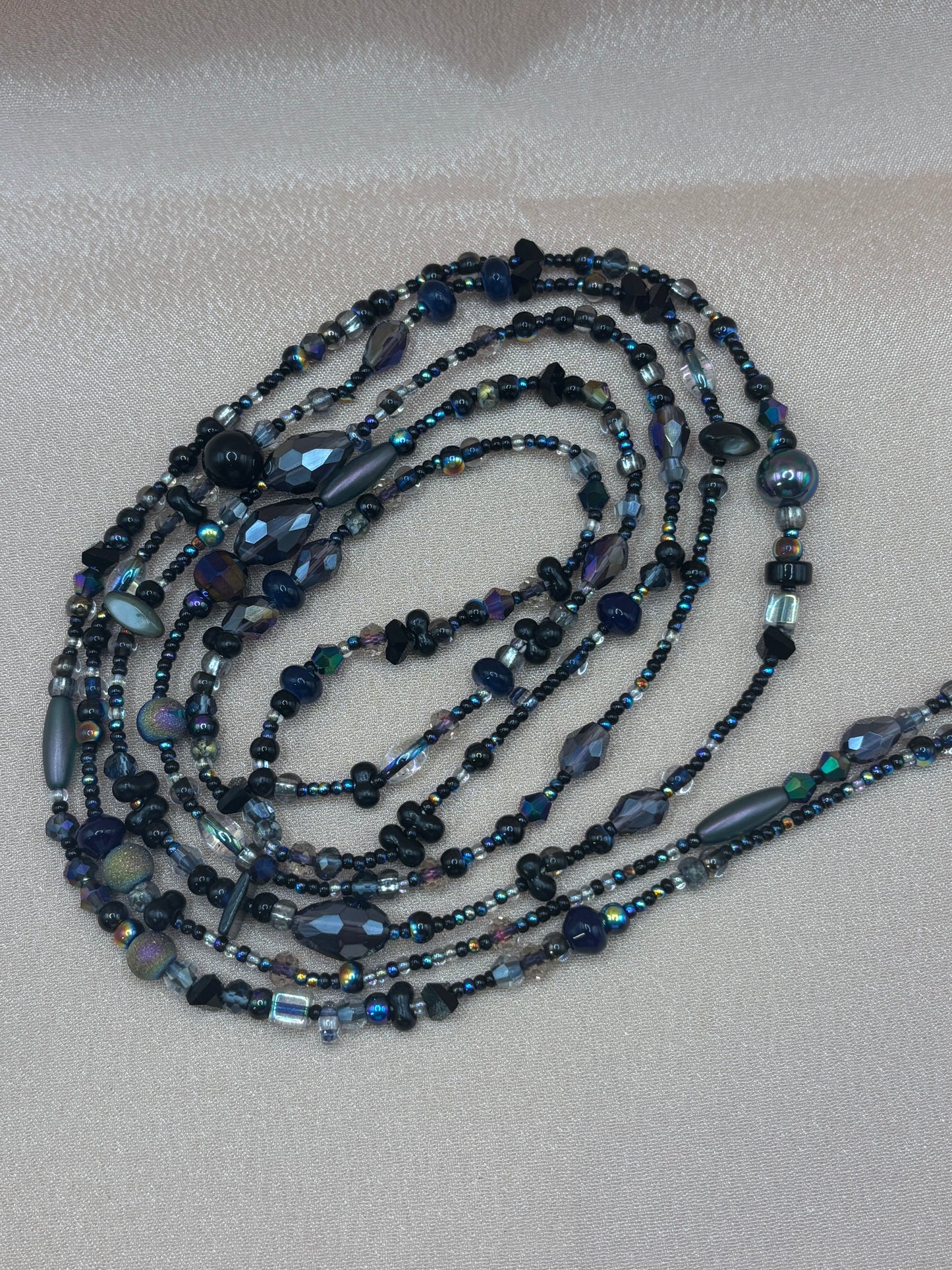 Handmade beaded waist beads featuring a dark blend of matte black, smokey grey crystals, and iridescent peacock-blue seed beads