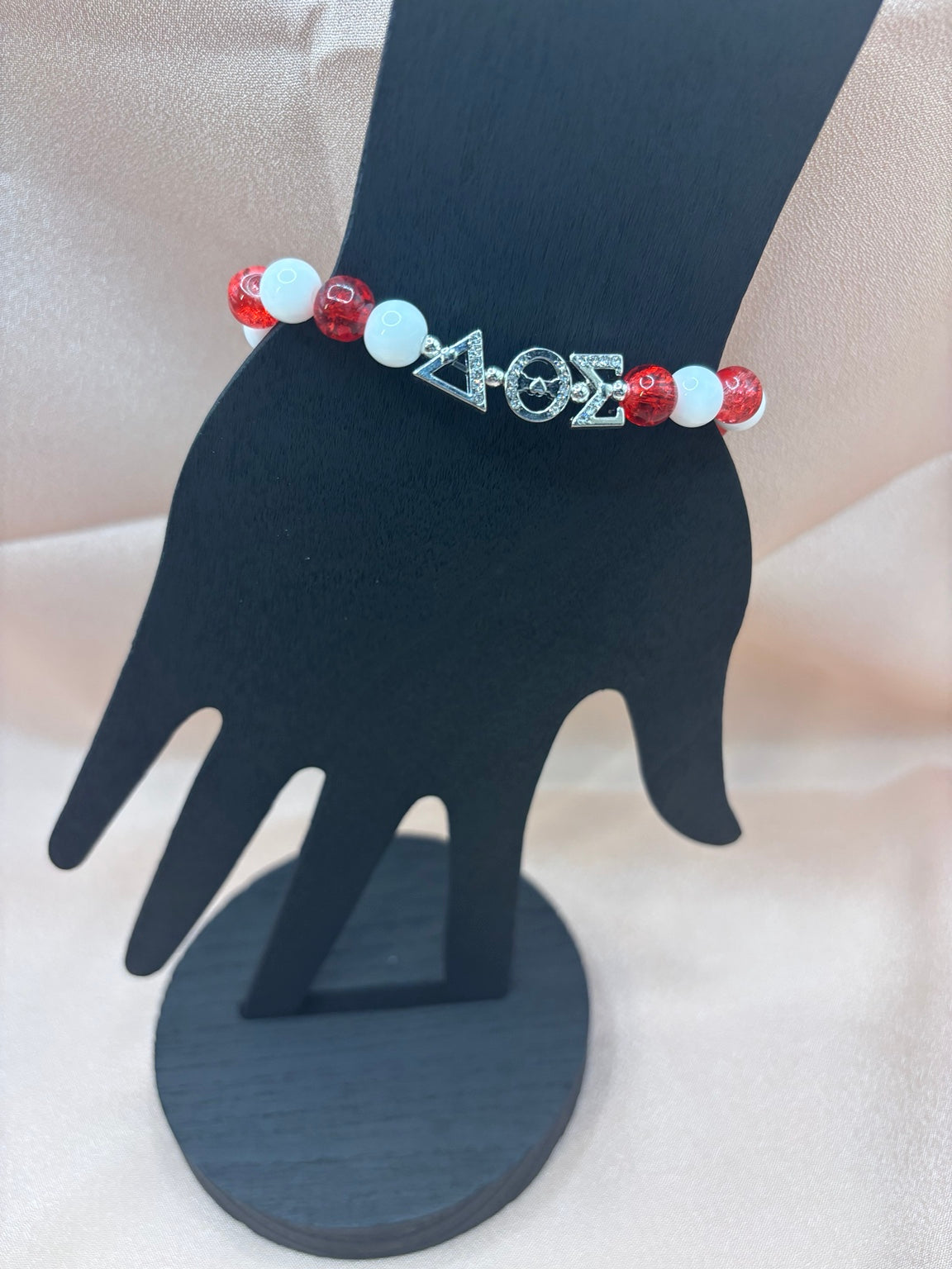Delta Sigma Theta inspired sorority bracelet on a display hand featuring red crackle beads, solid white beads, and silver Greek letter charms