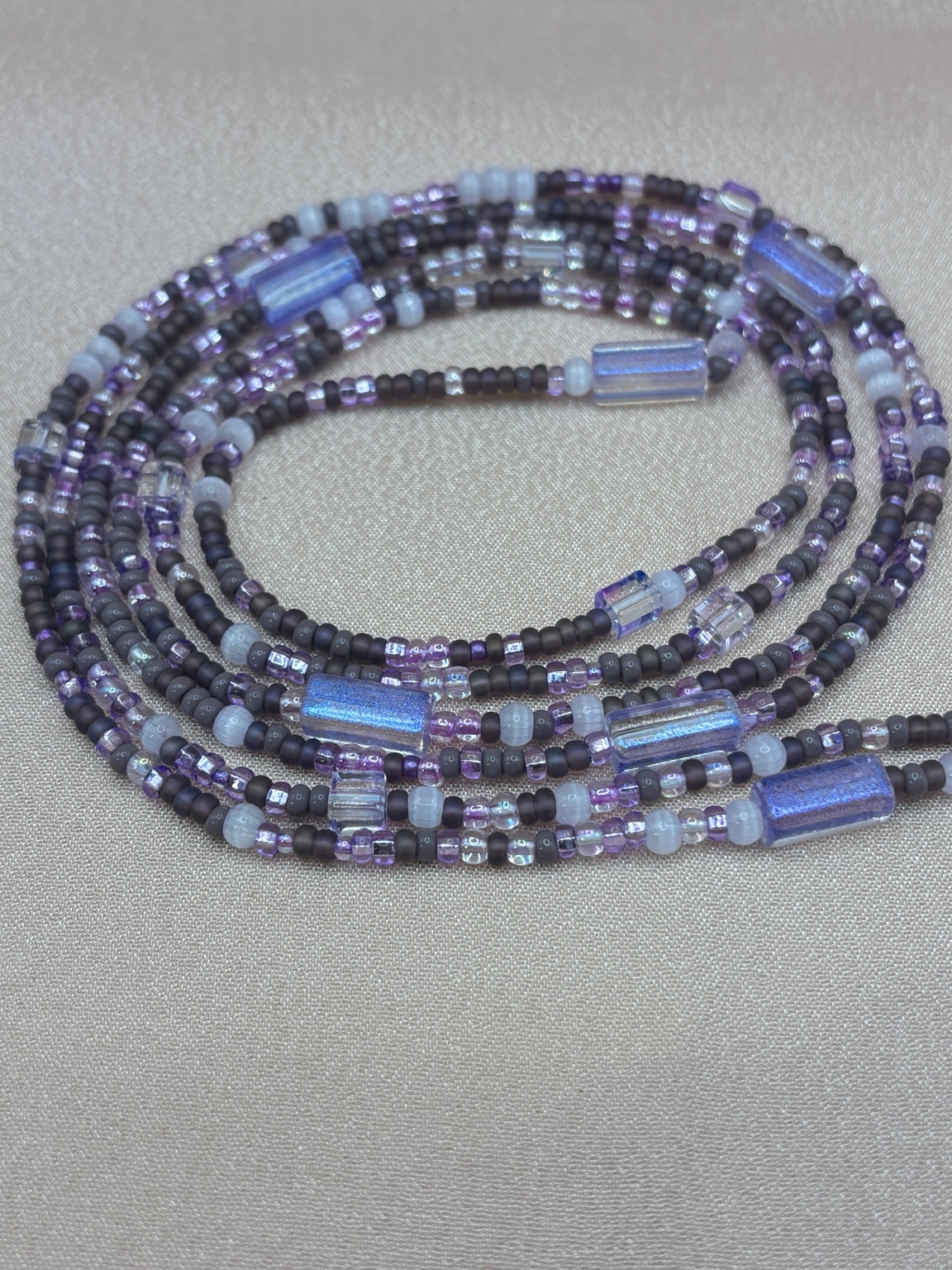 Handmade beaded waist beads in layers of matte dark purple, lilac, iridescent blue-purple tubes, and translucent seed beads